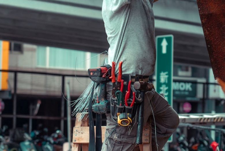 A guy on a ladder with a toolbelt secured around his waist.